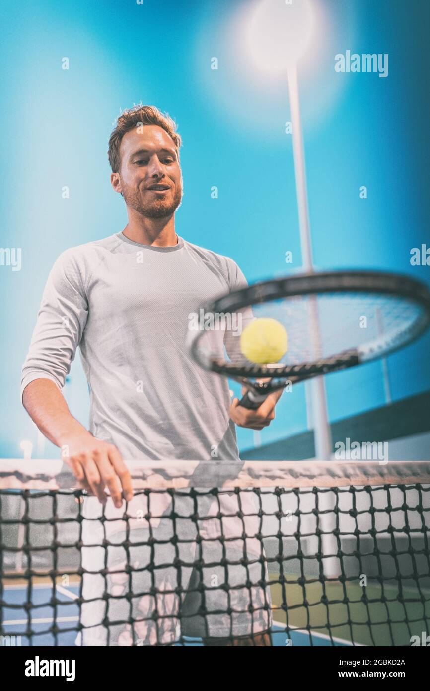 Mann Athlet Tennisspieler spielt auf dem Platz in der Nacht. Portrait am Netz mit Tennisschläger und Ball Stockfoto