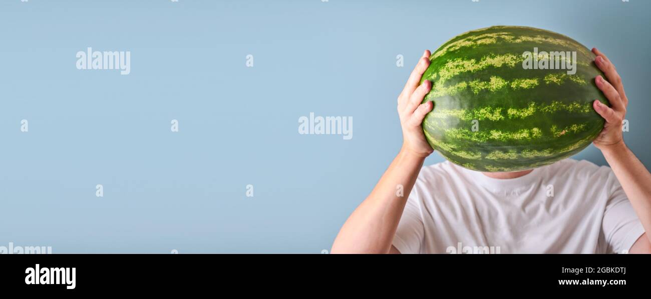 Junger Mann hält ganze Wassermelone in den Händen in weißem T-Shirt auf blauem Hintergrund. Design-Modell. Speicherplatz kopieren. Stockfoto