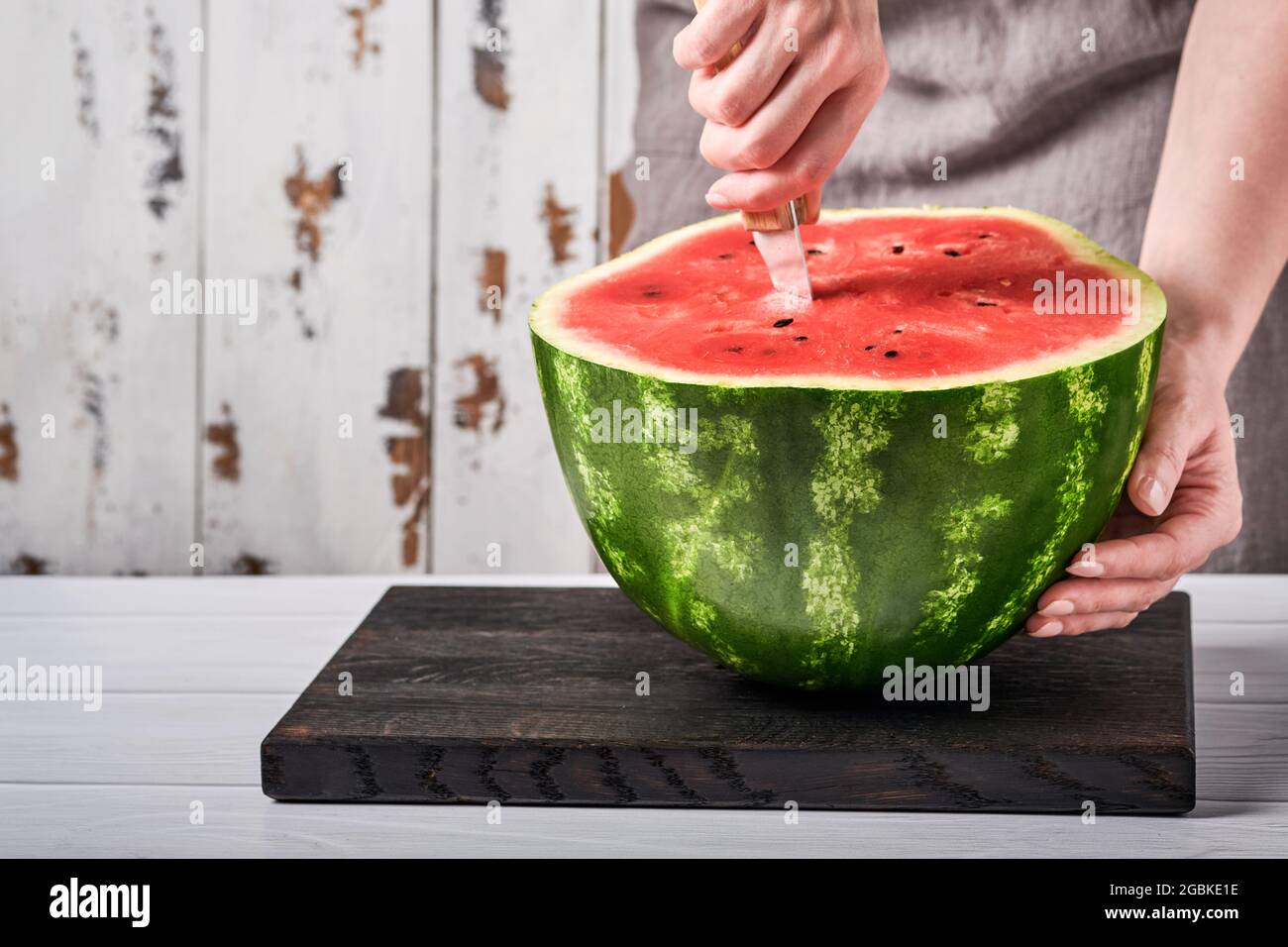 Weibliche Hände schneiden vor dem Hintergrund einer häuslichen Umgebung eine Wassermelone in Stücke. Selektiver Fokus. Stockfoto