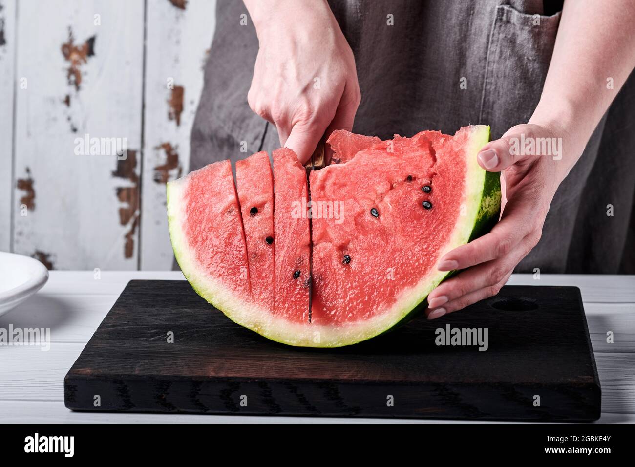 Weibliche Hände schneiden vor dem Hintergrund einer häuslichen Umgebung eine Wassermelone in Stücke. Selektiver Fokus. Stockfoto
