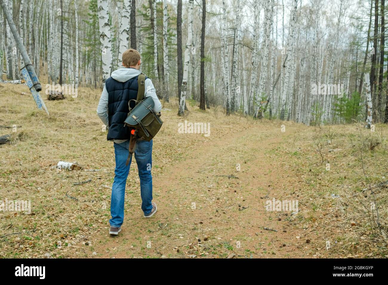 Ein Mann mit Rucksack geht im Frühjahr durch den Wald. Gelb verwelkte Blätter. Stockfoto