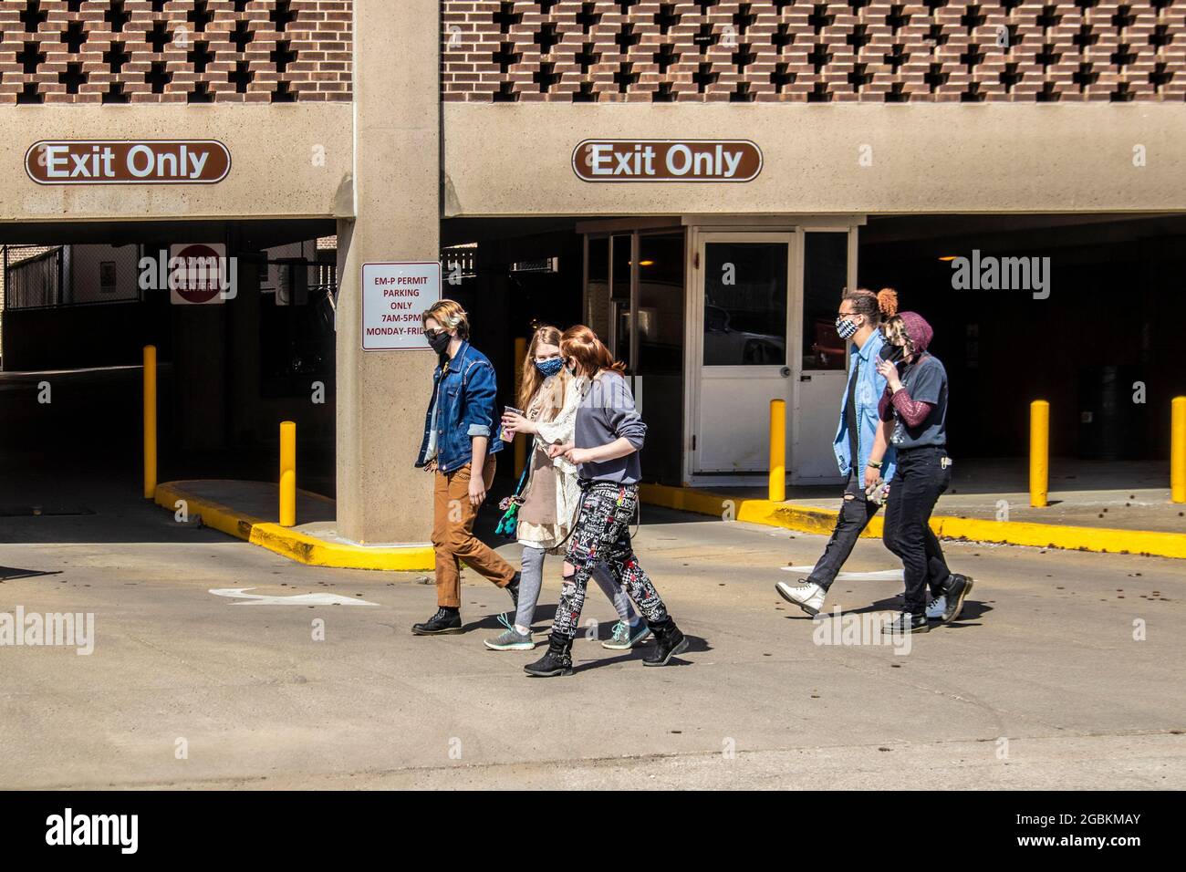 03 21 2021 Bloomington USA eine Gruppe von Universitätsstudenten mit Gesichtsmasken geht an sonnigen Tagen auf dem Bürgersteig durch die Parkgarage in der Nähe des Campus der IU Stockfoto
