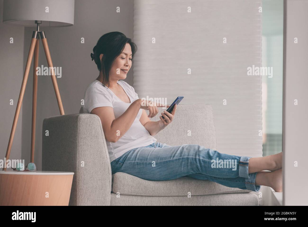 Arbeiten Sie von zu Hause aus glücklich asiatische reife Frau entspannen auf dem Sofa mit Handy Online-Shopping oder Remote-Arbeit Stockfoto