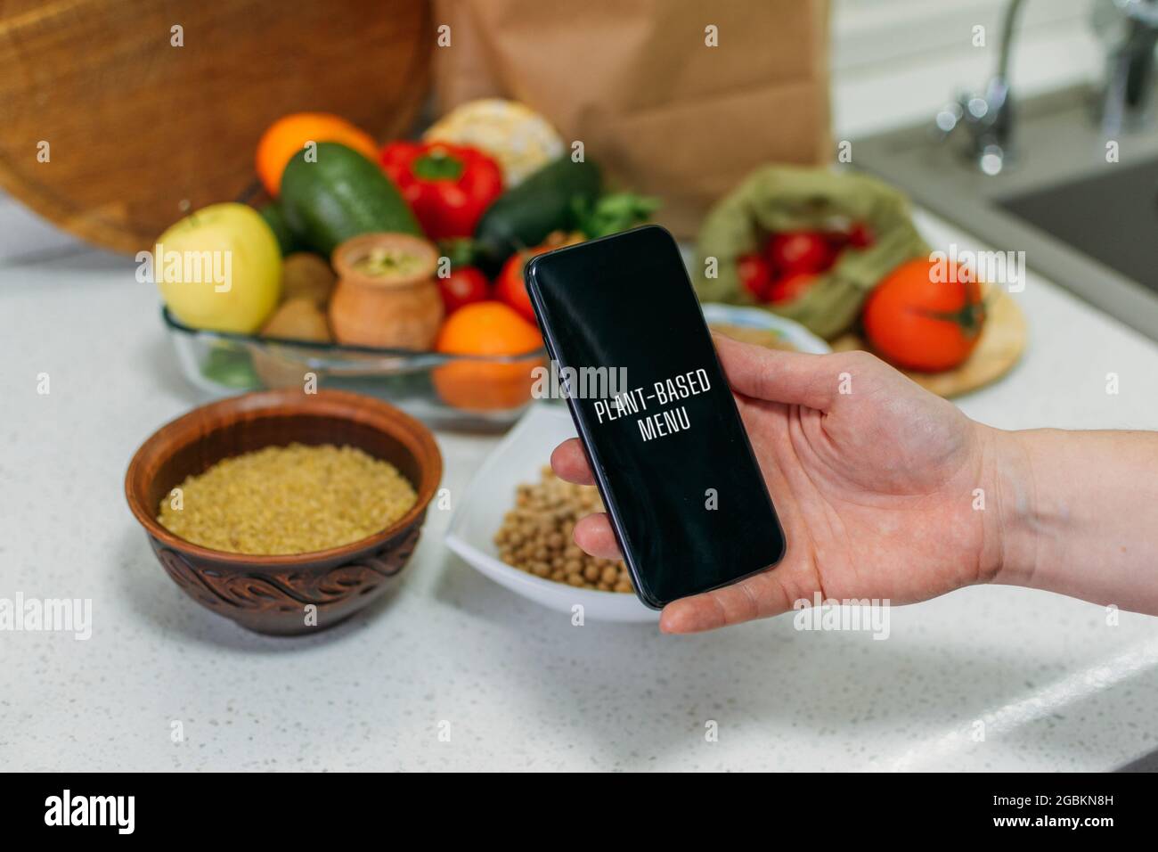 Ganznahrungsmittel, pflanzliche Ernährung für mehr Gesundheit. Weibliches Handtelefon mit pflanzlichen Menürezepten und gesunden Mahlzeiten, Gemüse, Obst, Vollkornprodukten Stockfoto