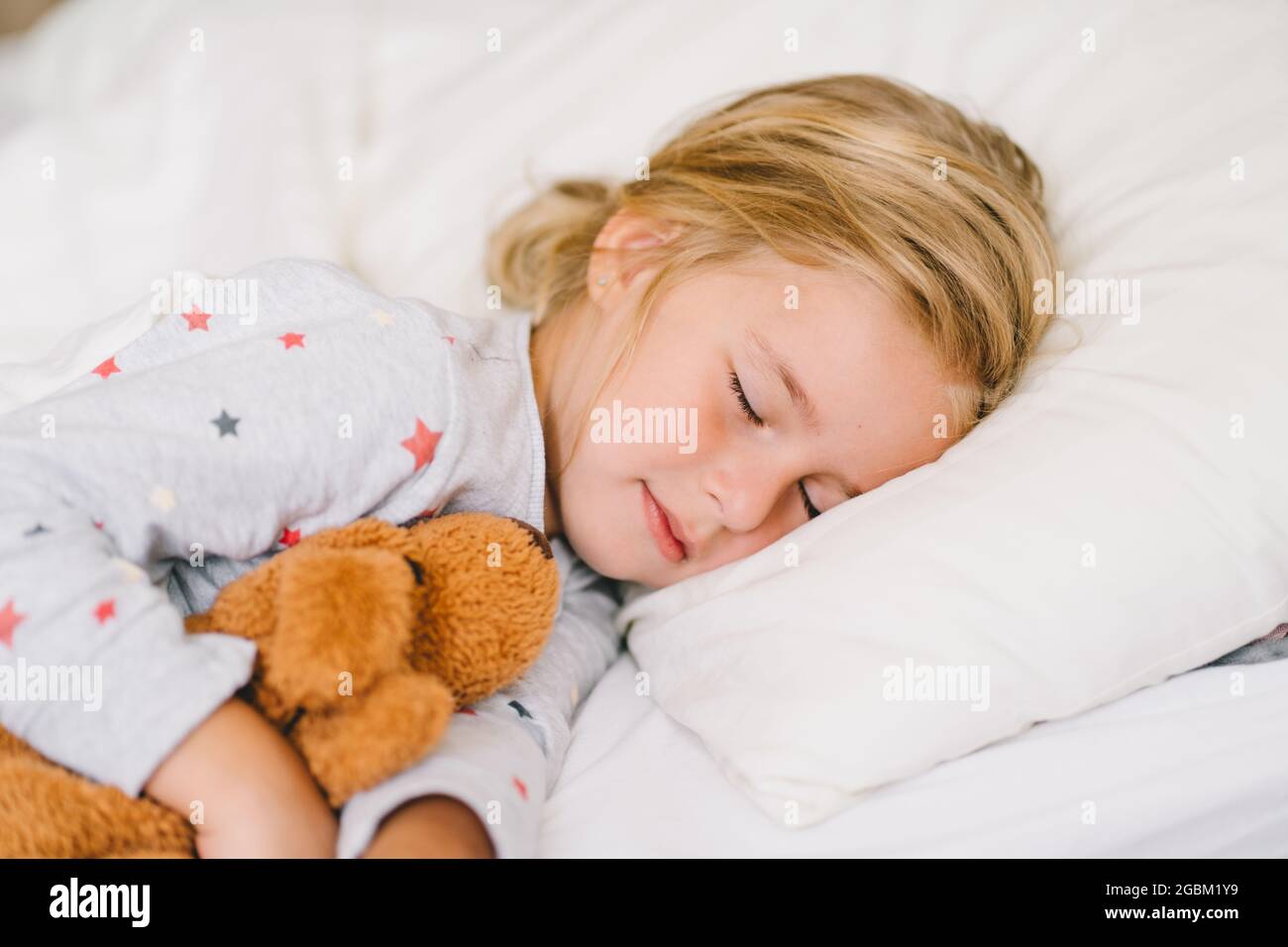 Kleinkind Mädchen im Schlafanzug schlafen auf weißen Bettwäsche und Umarmung Plüsch Spielzeug Stockfoto