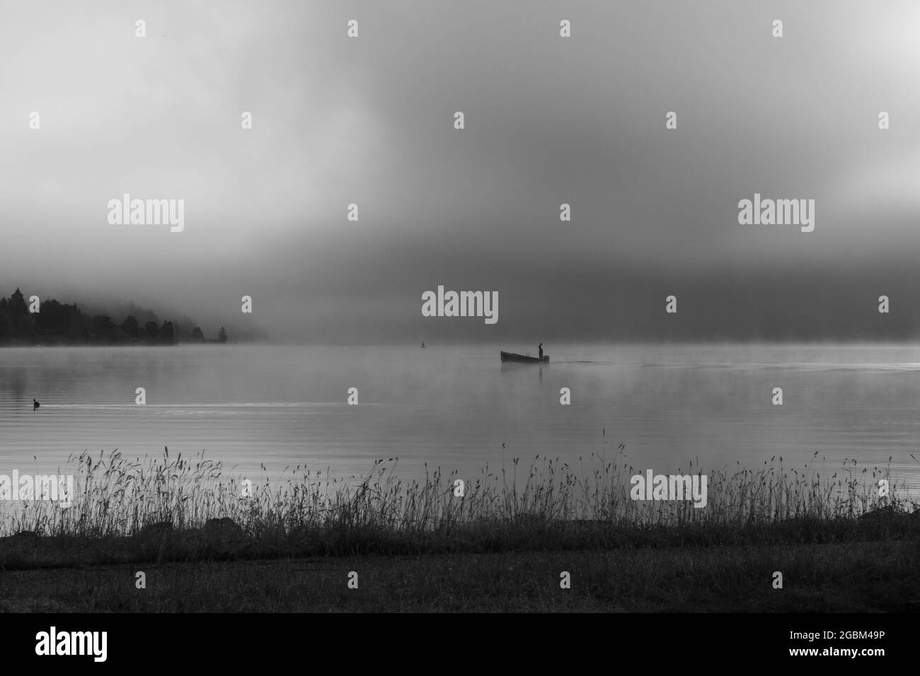 Ein früher Morgen am Lac de Joux, Schweiz: Ein einflüchtiger Fischer auf einem Boot, Nebel versteckt immer noch die aufgehende Sonne Stockfoto