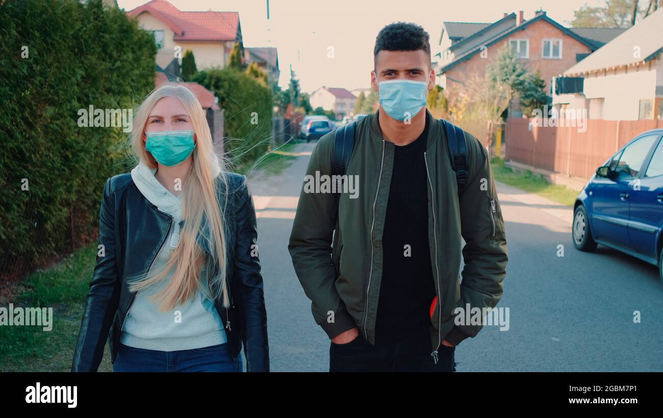 Multiethnische Mann und Frau in medizinischen Masken zu Fuß die Straße in Wohnimmobilien. Sie verbringen ihre Freizeit zusammen. Stockfoto