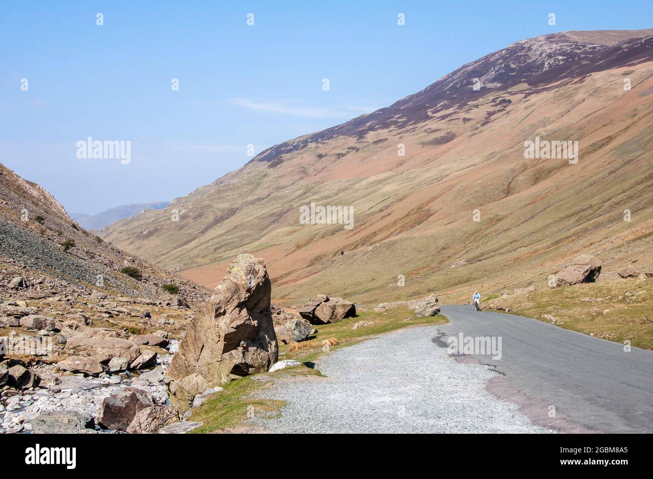 Ein Radfahrer klettert eine schmale Landstraße durch den Honister Pass unter den Bergen des englischen Lake District. Stockfoto