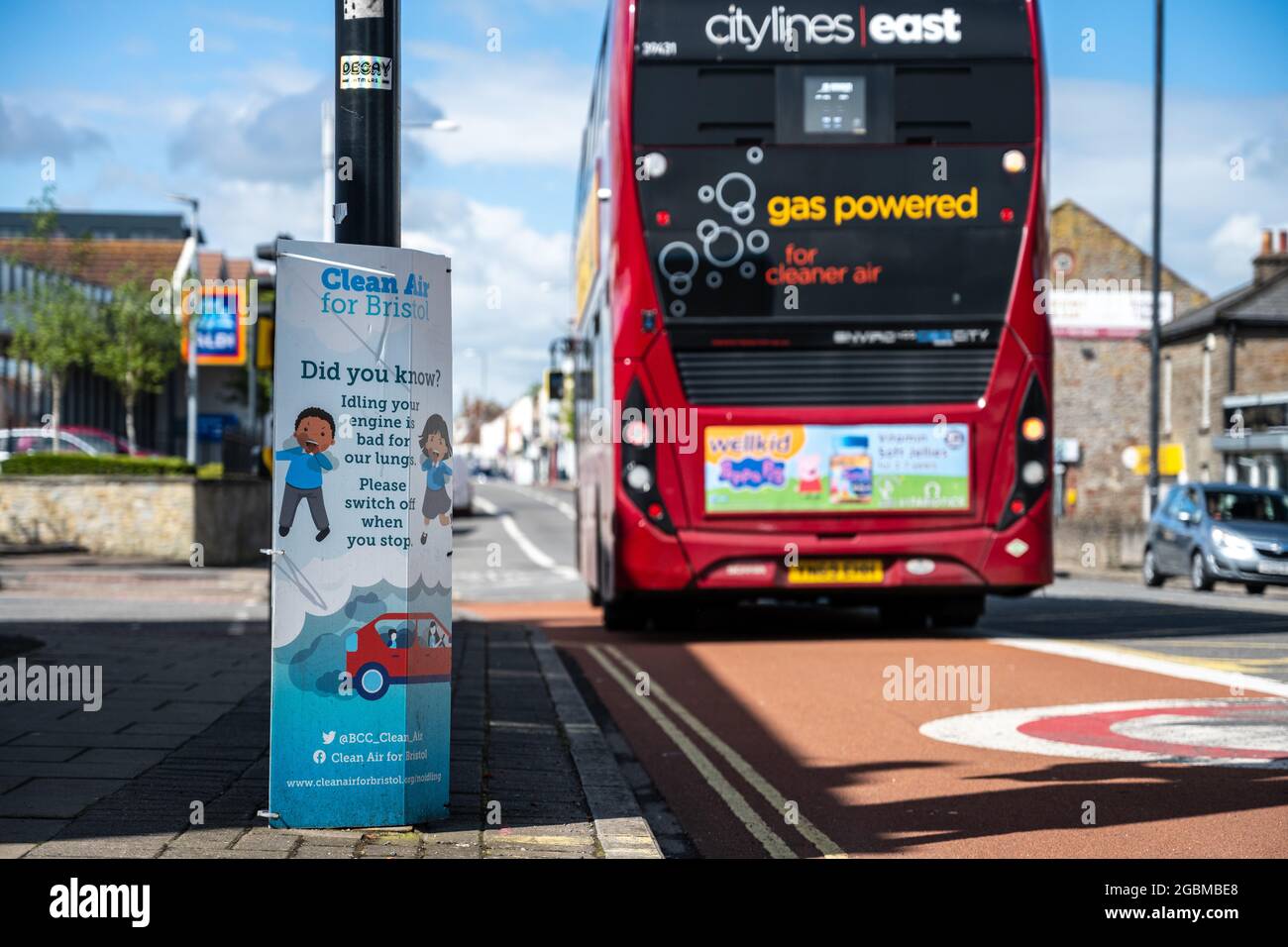 Ein Biogas-Bus fährt an einem „Clean Air“-Plakat vorbei, auf dem die Autofahrer aufgefordert werden, ihre Motoren im Leerlauf an einer Kreuzung an der Fishponds Road in Bristol abzuschalten. Stockfoto