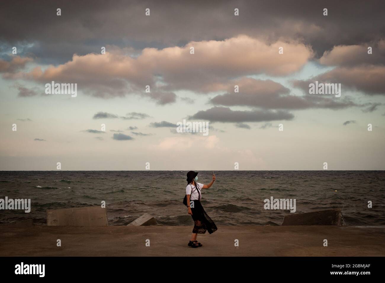 Eine Frau mit Gesichtsmaske nimmt nach einem stürmischen Tag in Barcelona ein Selfie auf einem Wellenbrecher auf. Stockfoto