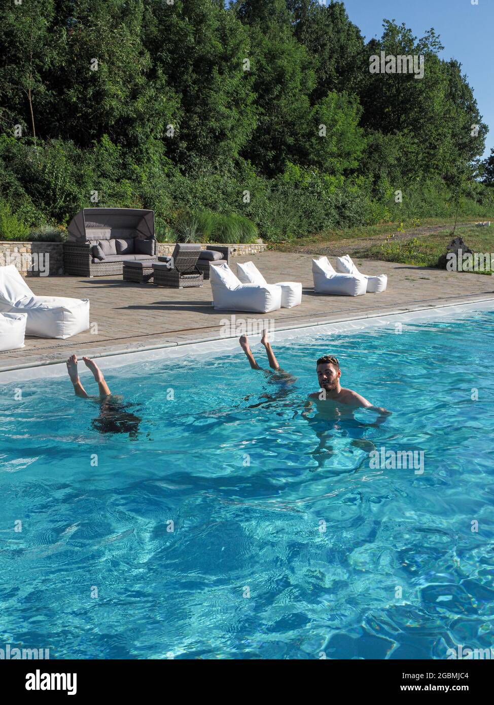 Vertikale Aufnahme eines kaukasischen Mannes im Pool mit zwei kopfüber stehenden Frauen an einem sonnigen Tag Stockfoto