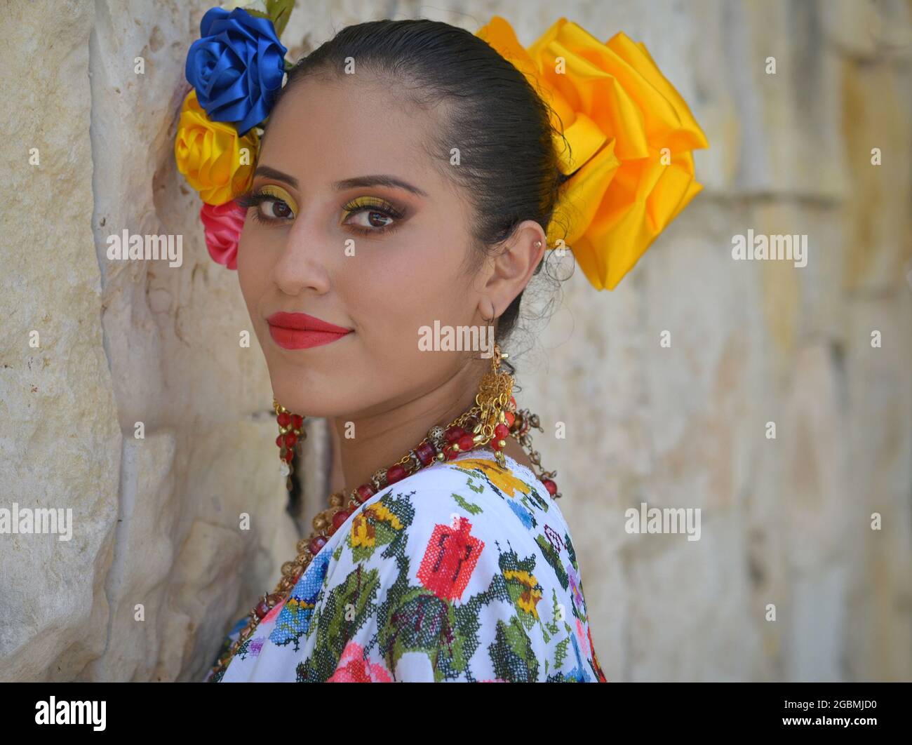 Die junge schöne mexikanische Yucatecan-Volkstänzerin trägt ein traditionelles folkloristisches Kleid mit bunten Blumen im Haar und blickt über ihre Schulter. Stockfoto