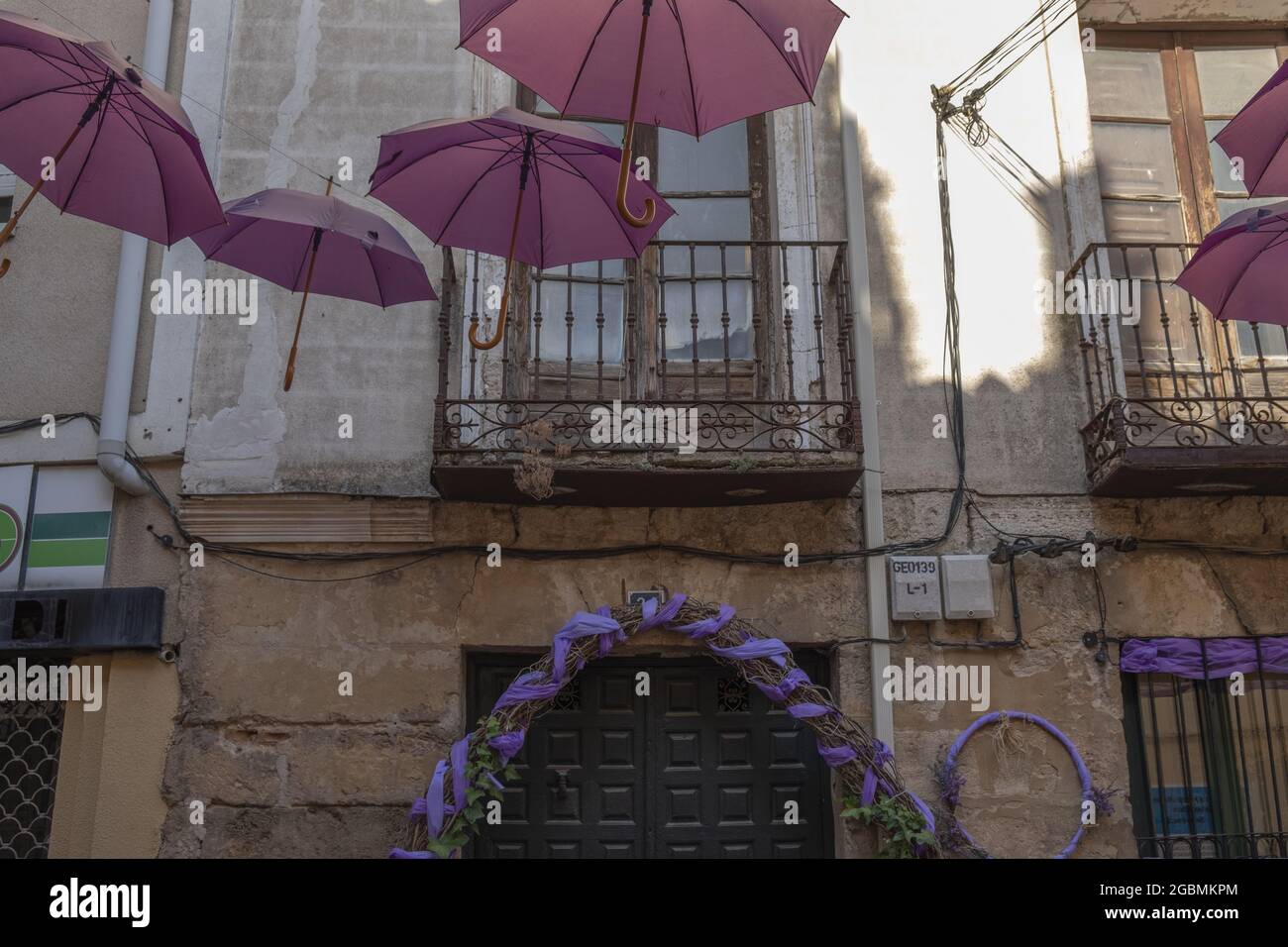 BRIHUEGA, SPANIEN - 10. Jul 2021: Die Reihen der purpurnen Schirme in den engen Straßen von Brihuega Stockfoto