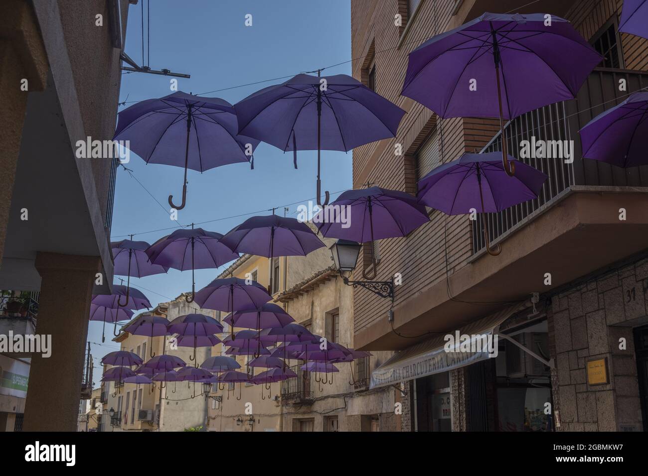 BRIHUEGA, SPANIEN - 10. Jul 2021: Die Reihen der purpurnen Schirme in den engen Straßen von Brihuega Stockfoto