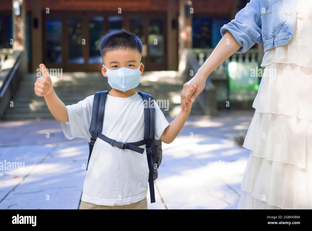 Mutter und Junge tragen Gesichtsmaske und gehen während des Coronavirus-Ausbruchs zur Schule. Stockfoto