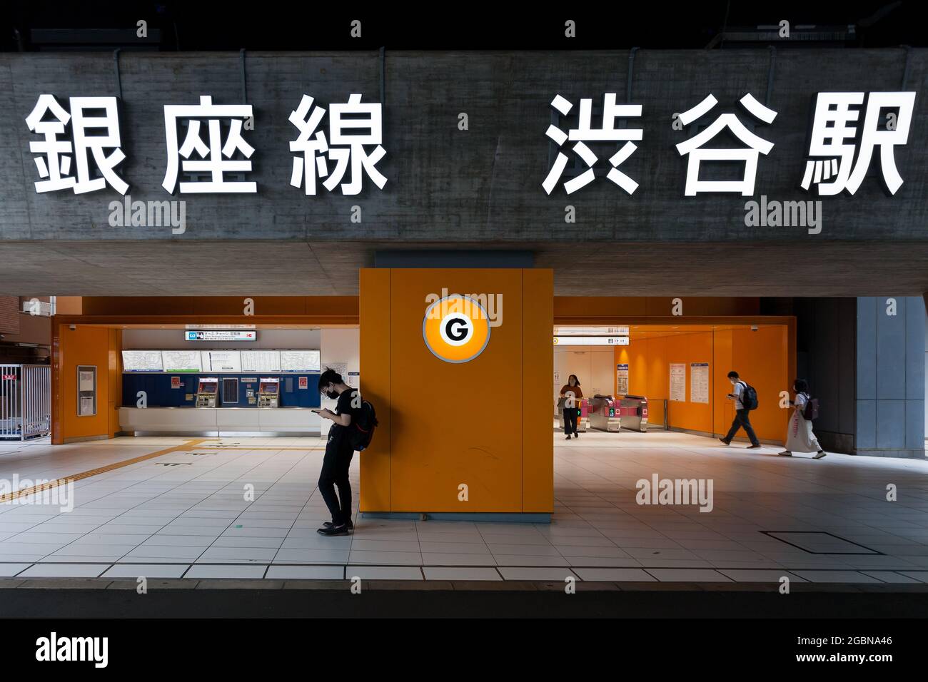 Ein junger Japaner, der eine Gesichtsmaske gegen COVID-19 trägt, überprüft sein Smartphone am Eingang der Ginza-Linie in Shibuya, Tokio, Japan. Stockfoto
