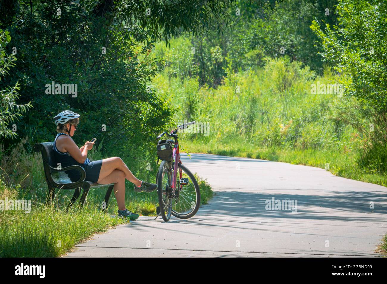 Die Fahrradfahrerin genießt den Sommertag, macht eine Pause vom Reiten, nutzt ihr Handy auf dem East Plum Creek Trail, Castle Rock Colorado US. Foto im Juli. Stockfoto