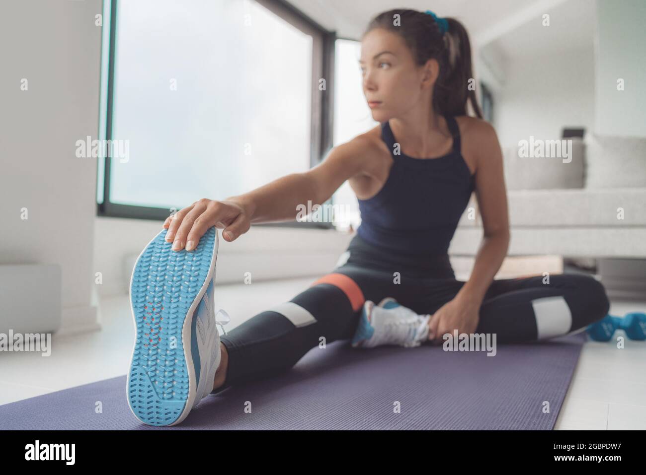Fitness zu Hause Asiatische Frau dehnt die Beinmuskeln auf einer Trainingsmatte für das Pilates- oder hiit-Training. Nahaufnahme von Laufschuhen Stockfoto