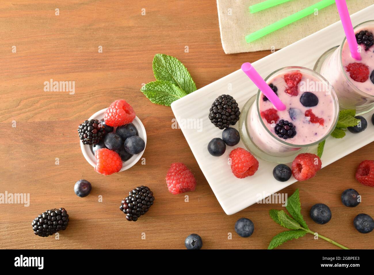 Waldfrucht-Smoothie mit Milch in Glasgläsern auf weißem Teller und Obst auf Holzbank. Draufsicht. Stockfoto