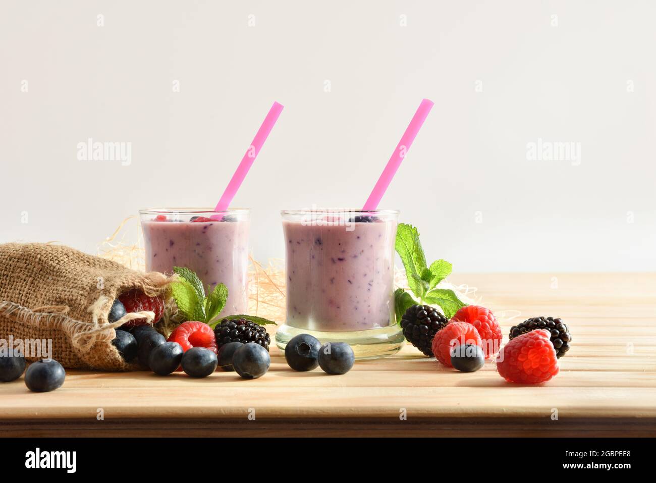 Waldbeerjoghurt Smoothie in Gläsern auf Holztisch mit Sack voller Heidelbeeren, Brombeeren Himbeeren weißen isolierten Hintergrund Stockfoto