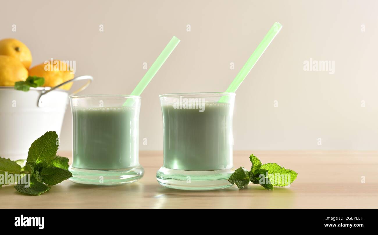 Zwei Gläser mit Milch mit Minze auf Holztisch mit Eimer mit Zitronen und isoliertem Hintergrund. Vorderansicht. Stockfoto
