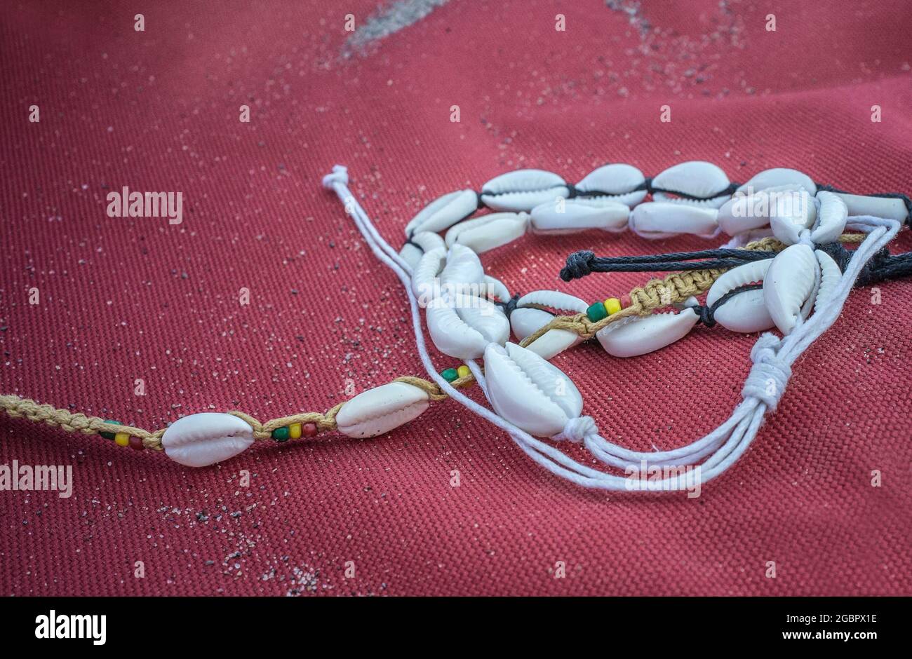 Shell-Knöchelarmband über rotem Segeltuch. Symbol der Sommerzeit Stockfoto