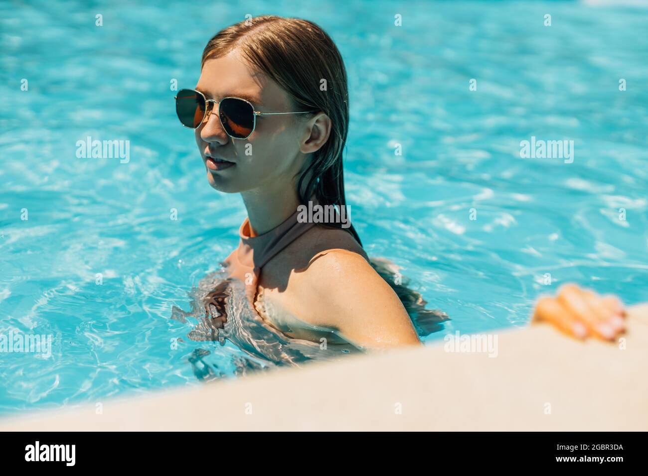 Schöne junge gebräunte Frau in Sonnenbrillen, im Außenpool, Frau in einem Badeanzug Sonnenbaden im Pool, glückliche Frau im Pool entspannen, die Con Stockfoto