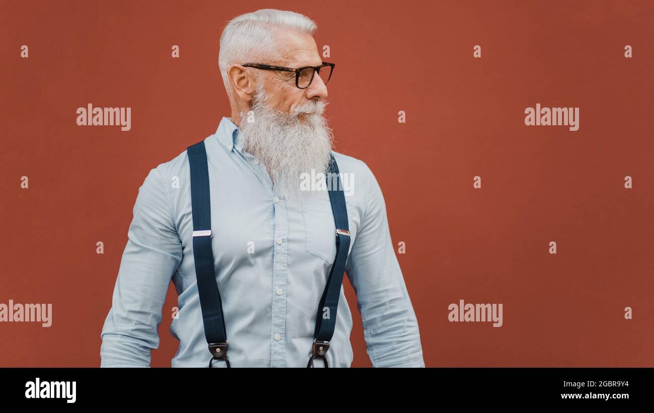 Älterer Mann mit Brille und modischem Kleid posiert auf rotem Hintergrund und sieht zur Seite Stockfoto