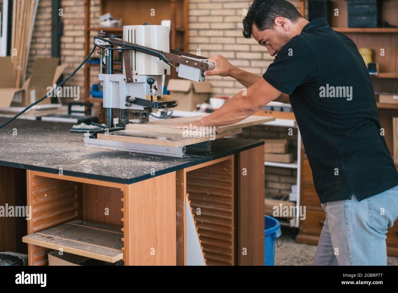 Mann, der in einer Werkstatt mit einer elektrischen Maschine eine Holzplatte schneidet. Stockfoto