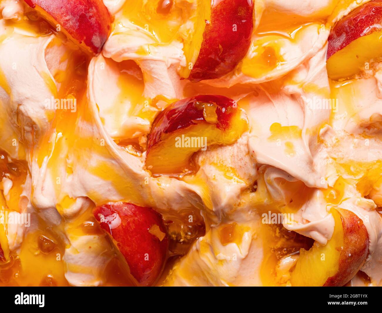 Frozen Peach Flavour Gelato - Vollformat Detail. Nahaufnahme einer beigefarbenen Oberflächenstruktur von Eiscreme, die mit orangeroten Früchten bedeckt ist. Stockfoto