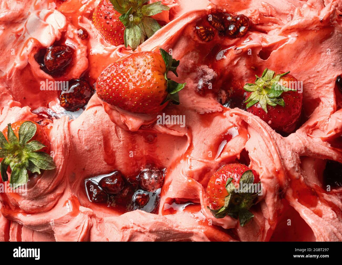 Frozen Strawberry Flavour Gelato - Vollformat Detail. Nahaufnahme einer rosa Oberflächenstruktur von Eiscreme, die mit roten Fruchtstücken bedeckt ist. Stockfoto