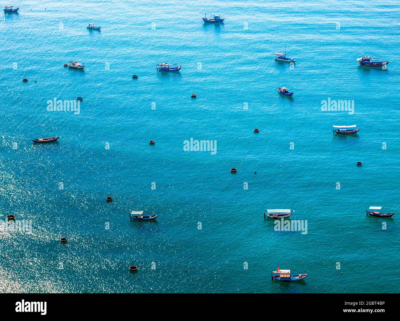 Kleine und große Boote vietnamesischer Seeleute im blauen Meer. Die linke Ecke ist die Spiegelung der Sonne auf dem Wasser Stockfoto