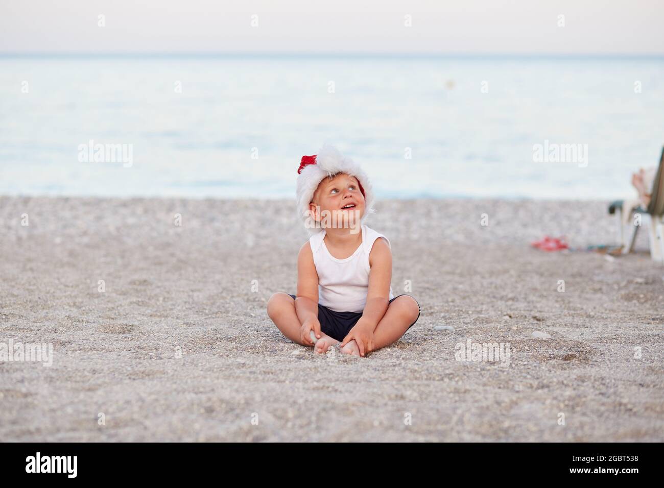 Der kleine kaukasische Junge feiert Silvester oder Weihnachten am Strand, am Meer. Urlaubskonzept, Weihnachtsstimmung. Hochwertige Fotos Stockfoto