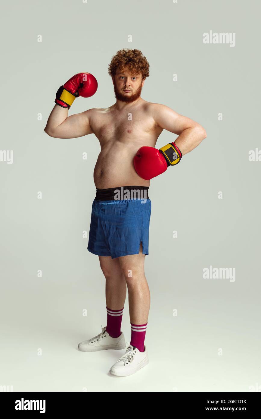 Lustiger rotköpfiger Mann in blauen Boxshorts und Handschuhen isoliert auf grauem Studiohintergrund. Konzept von Sport, Humor und Körper positiv. Stockfoto