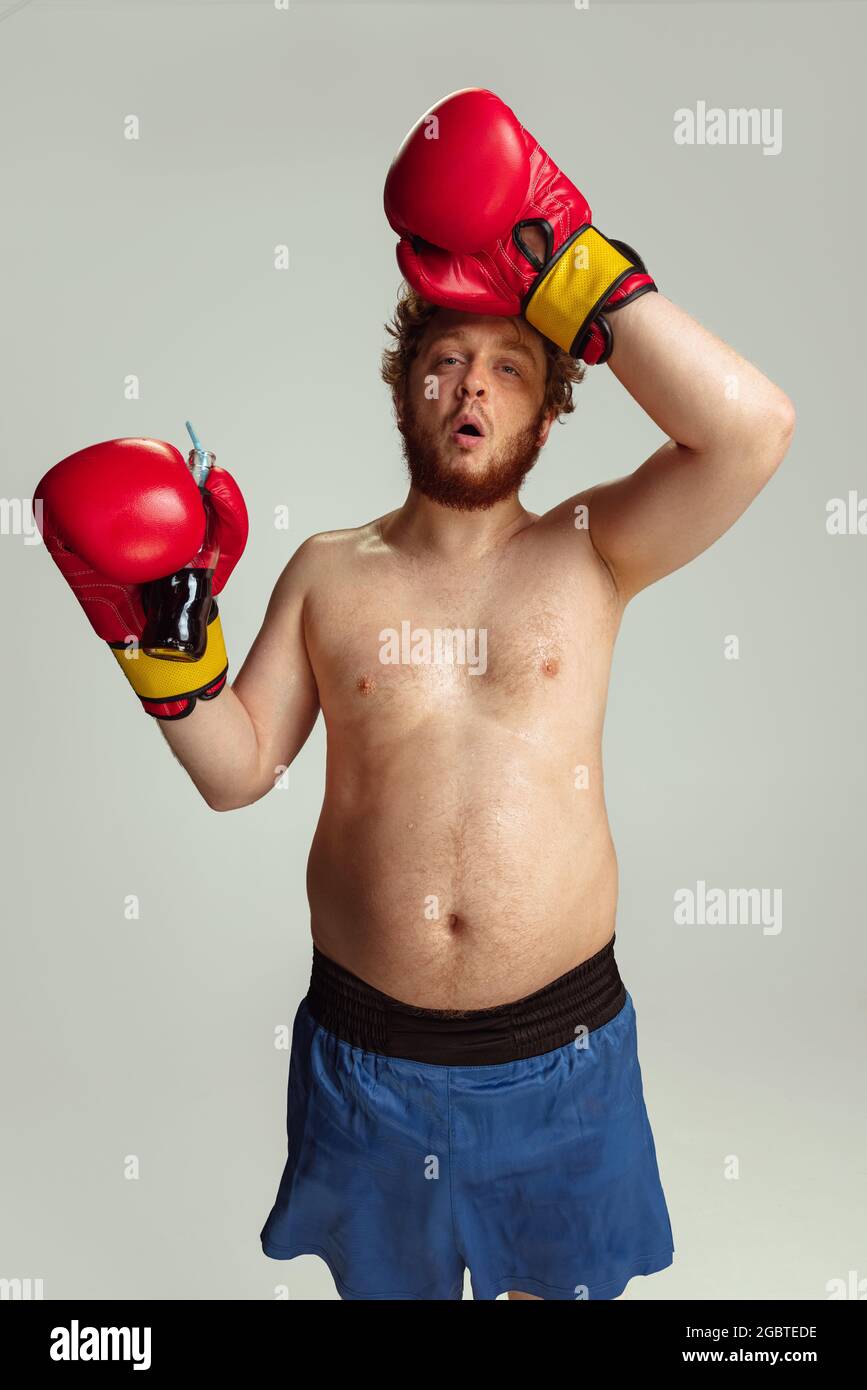 Lustiger rotköpfiger Mann in blauen Boxshorts und Handschuhen isoliert auf grauem Studiohintergrund. Konzept von Sport, Humor und Körper positiv. Stockfoto