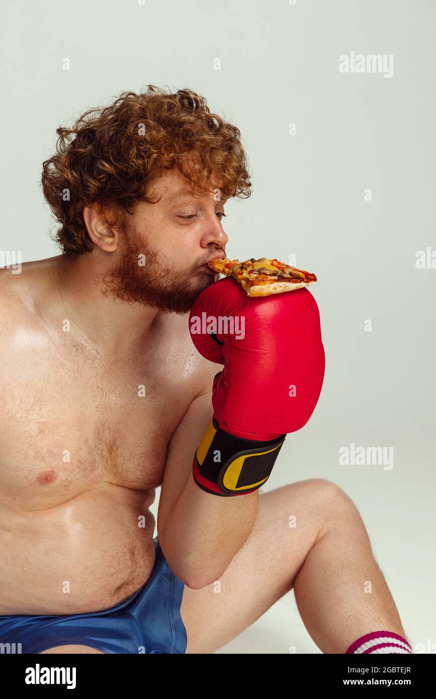 Lustiger rotköpfiger Mann in blauen Boxshorts und Handschuhen isoliert auf grauem Studiohintergrund. Konzept von Sport, Humor und Körper positiv. Stockfoto