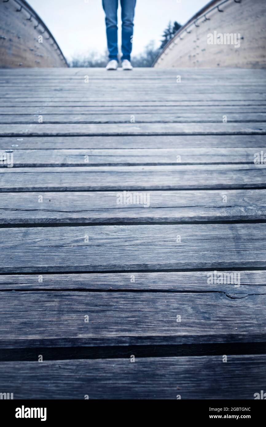 Unbekannte Person in Jeans und weißen Sneakers, die auf einer Holzbrücke steht Stockfoto