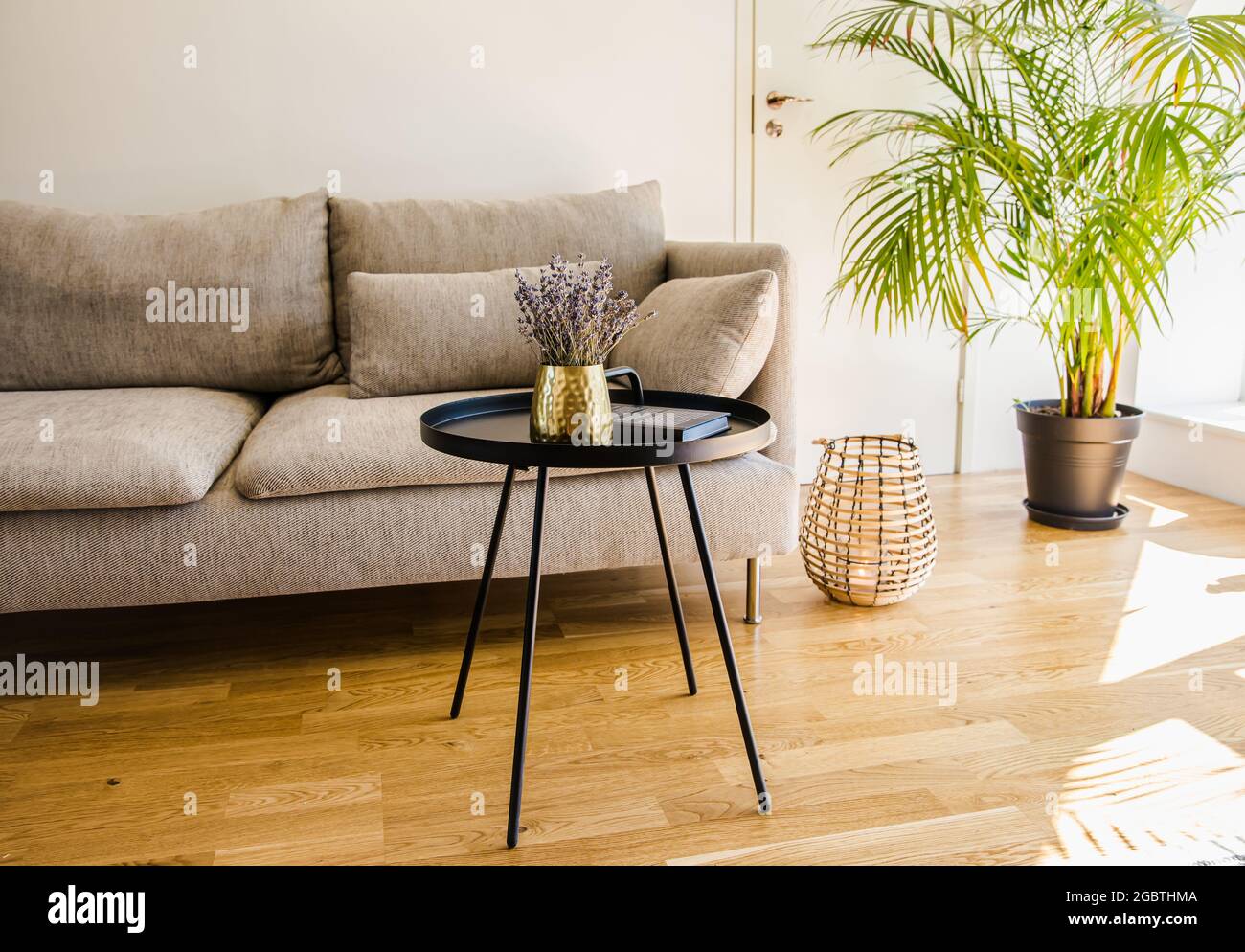 Minimalistisches, modernes Wohnzimmer mit schwarzem Akzent, Tisch mit Goldvase und schwarzem Metalltisch auf natürlichem Eichenholzboden. Stockfoto