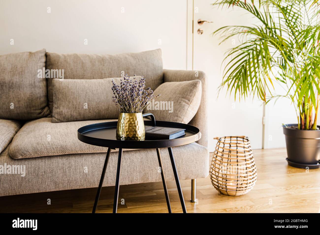 Minimalistisches, modernes Wohnzimmer mit schwarzem Akzent, Tisch mit Goldvase und schwarzem Metalltisch auf natürlichem Eichenholzboden. Stockfoto
