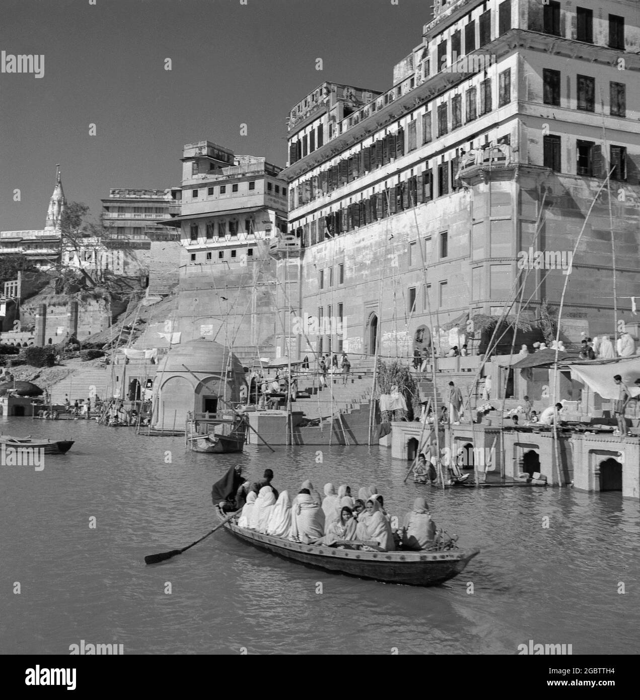 In den 1950er Jahren, geschichtlich, drängten sich Menschen in einem kleinen hölzernen Ruderboot auf dem Ganges-Fluss, Bernares, Indien. Der Fluss zieht Tausende von Pilgern zum Baden an seine Ufer, da sie als heilige Gewässer gelten. Stockfoto