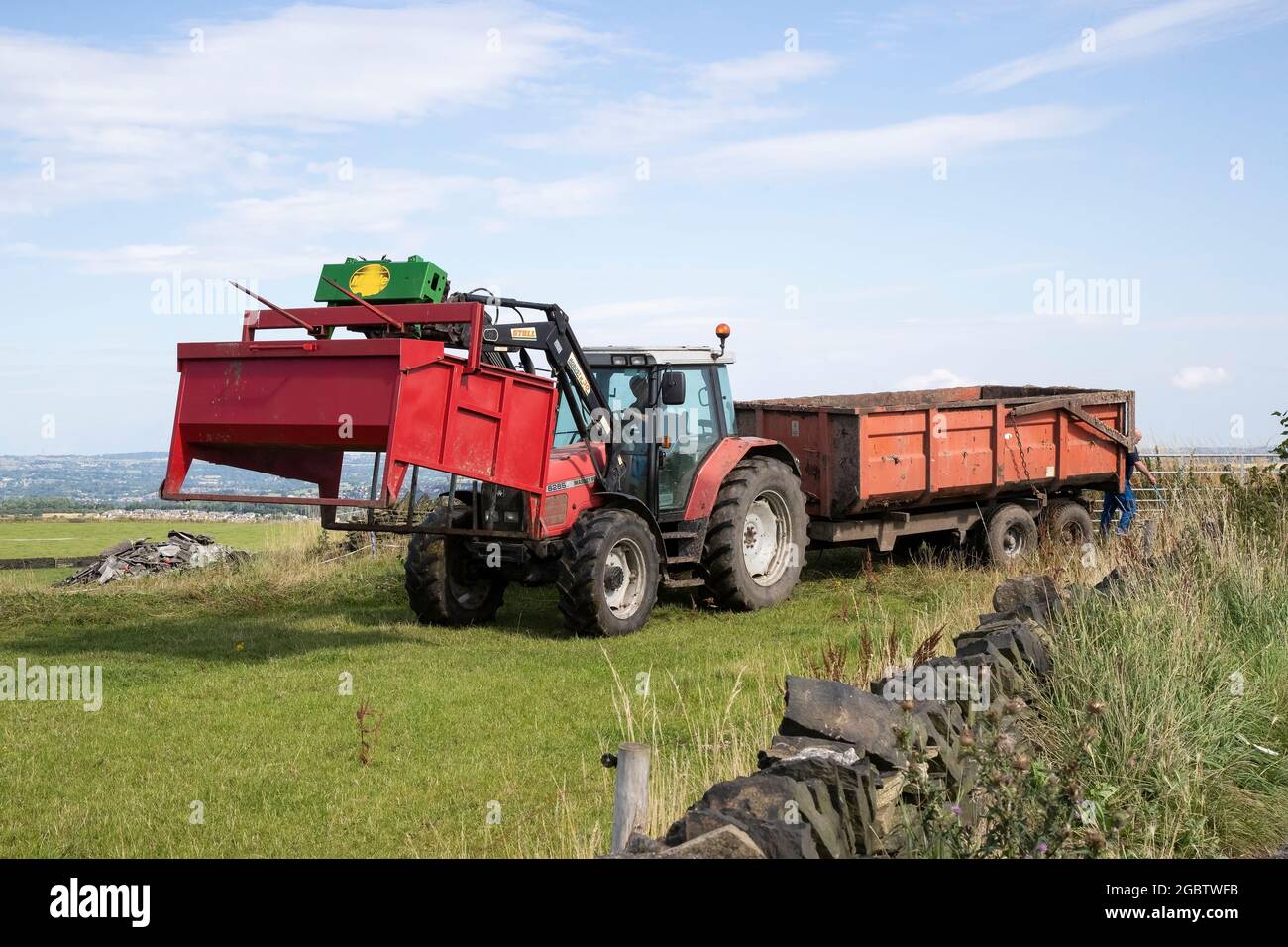 Massey Ferguson 6265 Traktor mit Anhänger und Ballenaufsatz, der im Sommer auf einer Hochlandfarm in West Yorkshire ein Feld mit Trockenmauern begibt Stockfoto