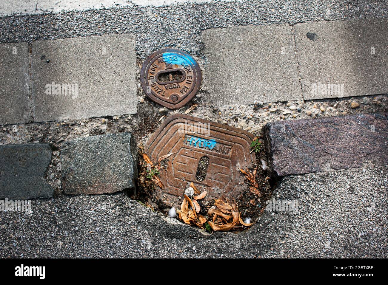 Nahaufnahme einer Schachtabdeckung, Hydrant in Grauen Kiessteinen für die Bauindustrie. Hintergrund für geometrische Formen. Verrostete Abdeckung auf der Straße. Straßenverkehrsskons Stockfoto