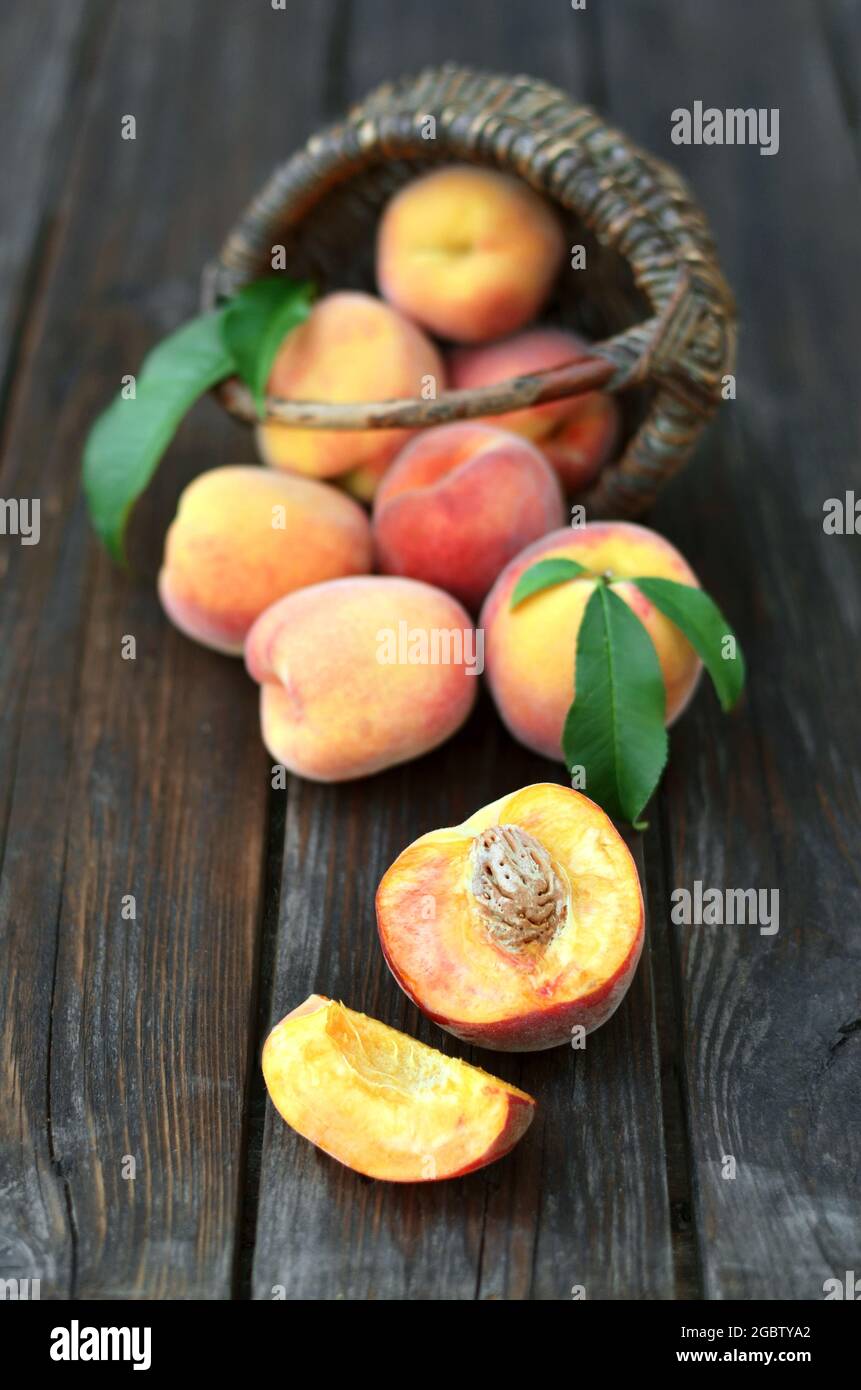 Nahaufnahme von frischen, saftig reifen Pfirsichen, die neben einem Korbkorb auf einem alten Holztisch verstreut sind, selektiver Fokus am unteren Bildrende. Gesunde Ernährung Stockfoto