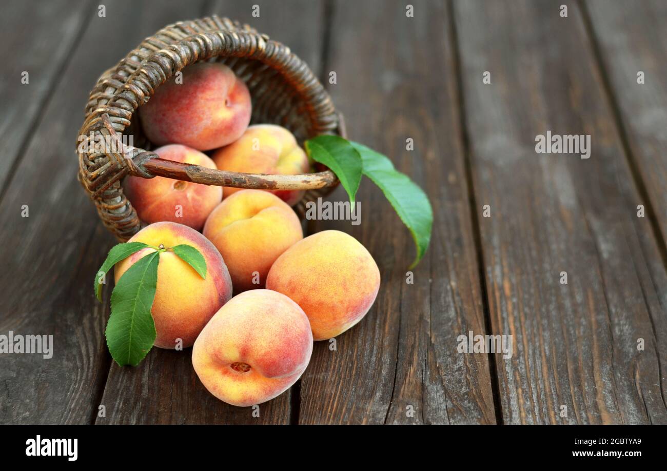 Frische saftige reife Pfirsiche in einem umgedrehten Weidenkorb auf einem alten Holztisch, selektiver Fokus am unteren Bildrende. Gesunde Ernährung Konzept. Stockfoto
