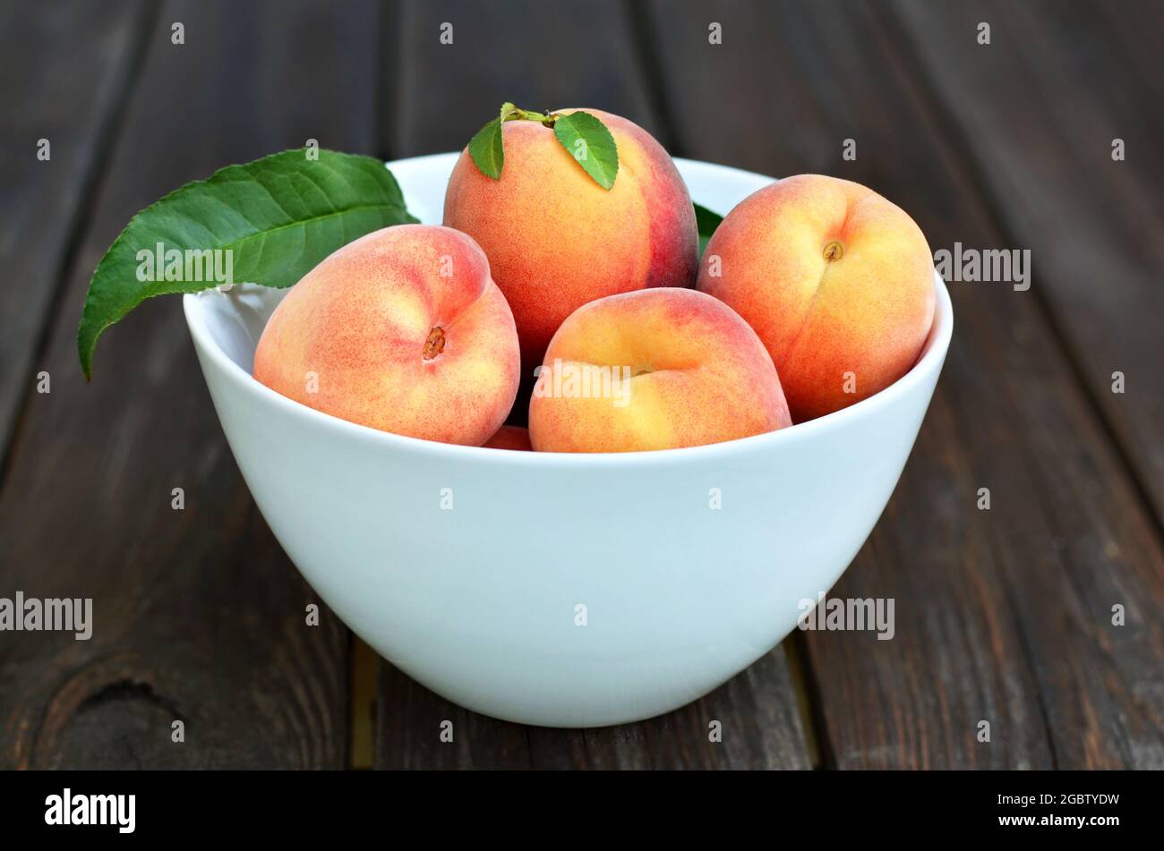 Weiße Schale mit reifen Pfirsichfrüchten auf einem rustikalen Holztisch. Gesunde Ernährung Konzept. Stockfoto