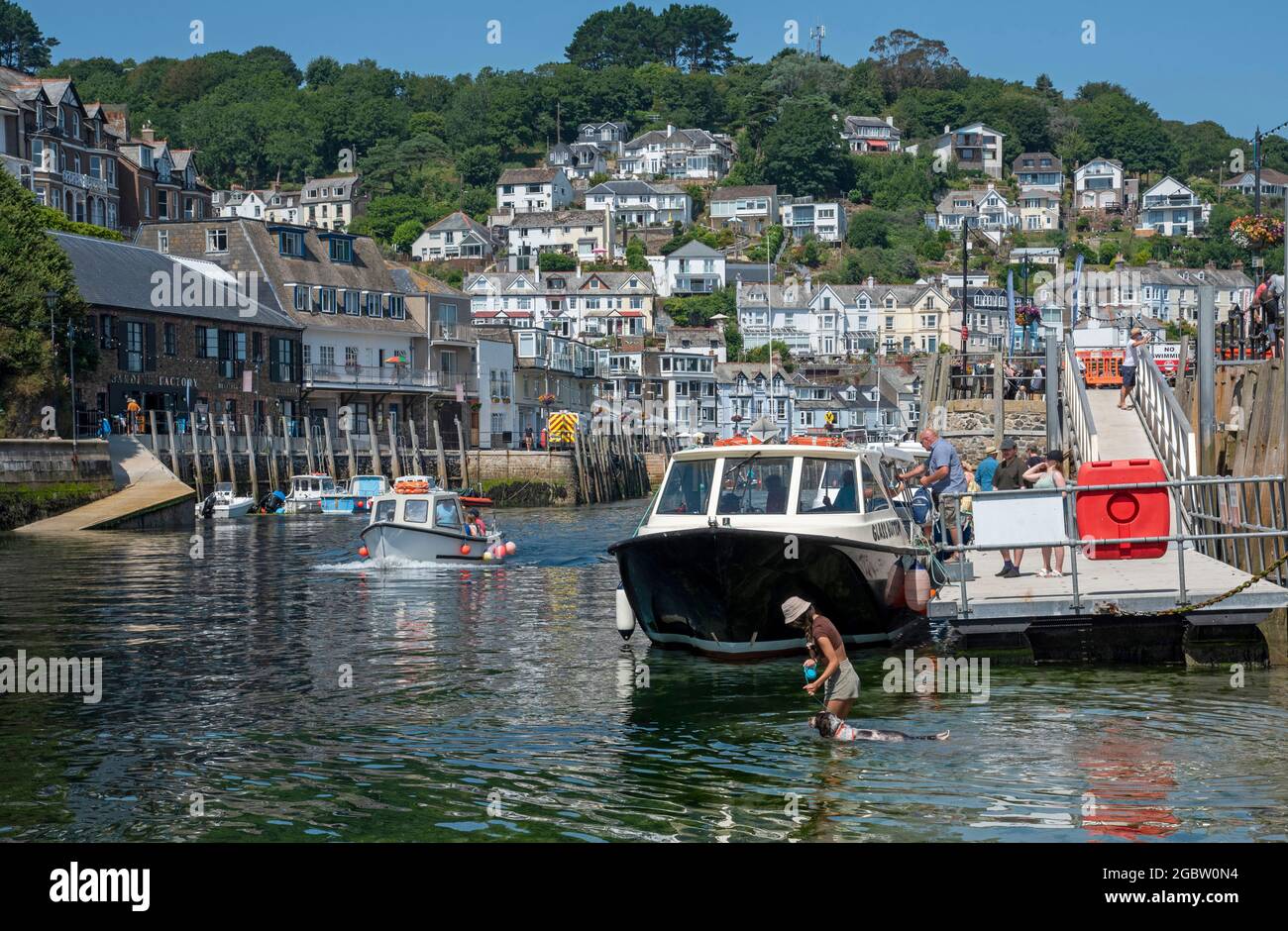 Looe, Cornwall, England, Großbritannien. 2021. Urlauber, die eine Bootsfahrt besteigen und eine Frau mit ihrem Hund im Hafen bei ankommender Flut. Stockfoto