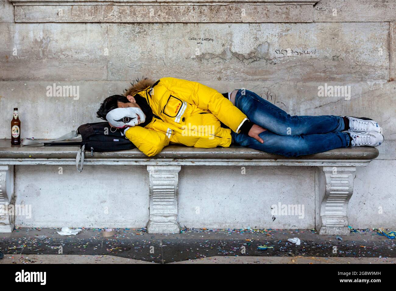 Ein junger Mann schläft auf EINER Bank auf dem Markusplatz während des Karnevals in Venedig, Italien. Stockfoto