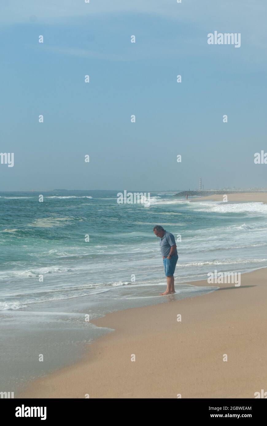 Einsamer Mann, der am Strand steht, als das Meerwasser seine Füße erreicht, Portugal, Costa Nova, 10.06.2021 Stockfoto
