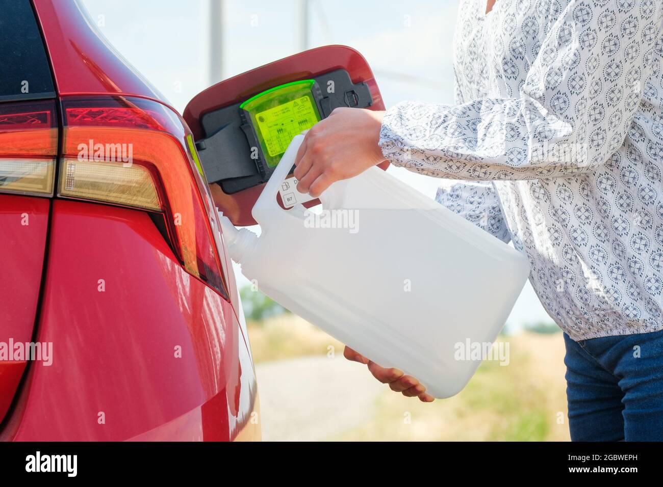 Nahaufnahme Frau, die das rote Auto mit Kraftstoff oder einer Dieselmotorflüssigkeit aus dem Behälter auf dem Feld befüllt. Stockfoto