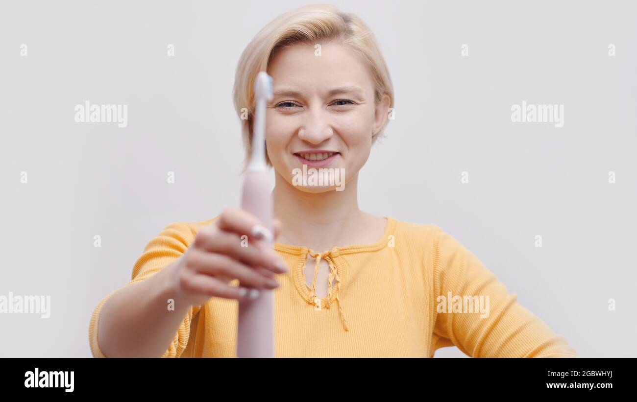 Nettes Mädchen mit einer elektrischen Ultraschallzahnbürste. Mädchen in einem gelben Top gekleidet. Morgendliche Routine. Zahnpflege. Konzept der persönlichen Hygiene. Isolierte Aufnahme über weißem Hintergrund im Studio. Stockfoto